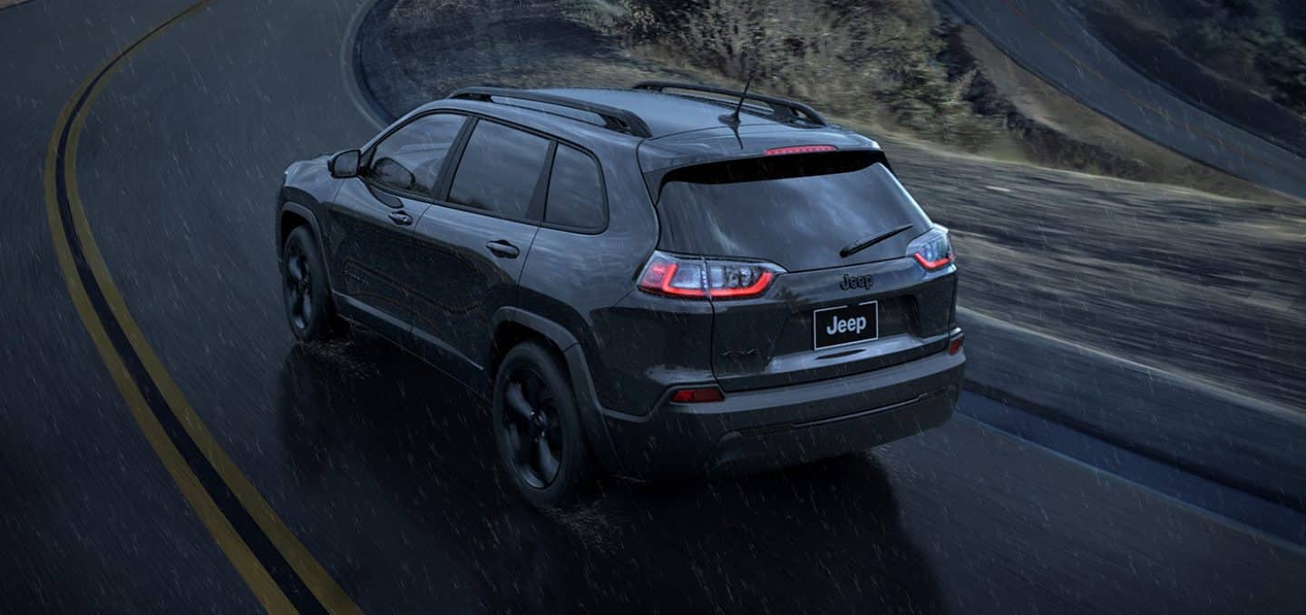 Display An angled rear view of a 2023 Jeep Cherokee Altitude Lux being driven on a curve in a rainstorm.
