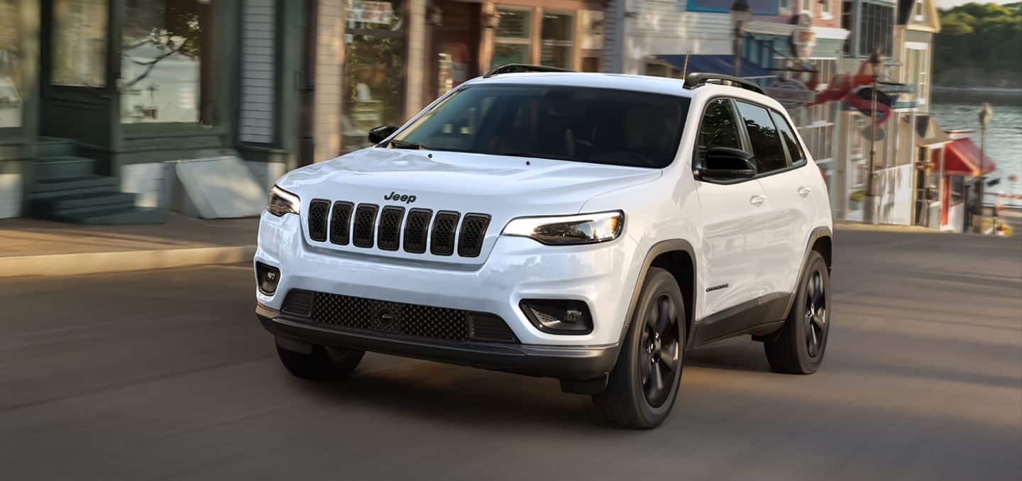 Display A white 2023 Jeep Cherokee Altitude Lux being driven on a city street.
