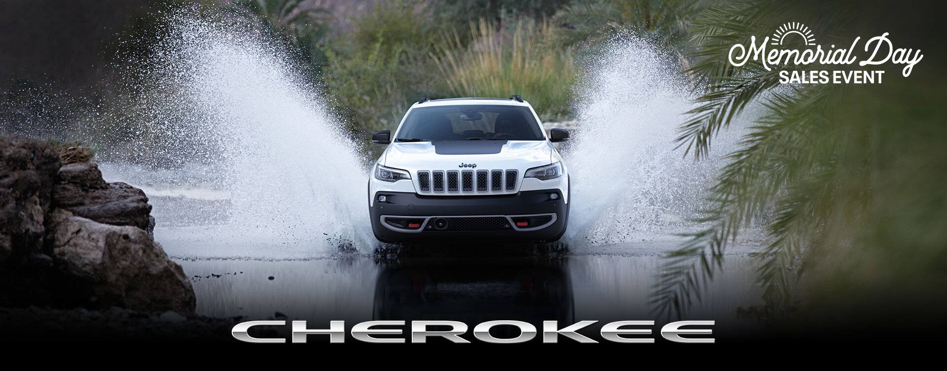 A head-on angle of a white 2023 Jeep Cherokee Trailhawk fording a stream off-road, with water splashing well above the top of the vehicle. Cherokee. The Memorial Day Sales Event logo.
