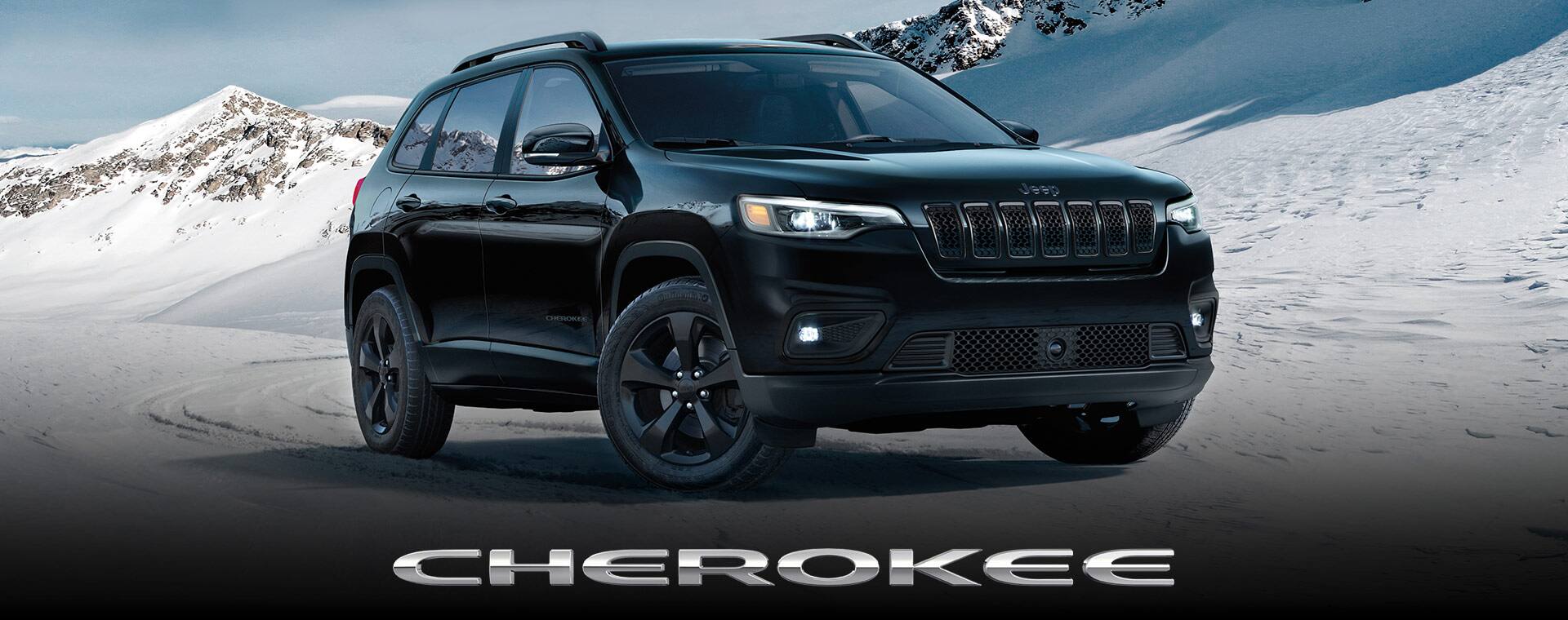 A 2023 Jeep Cherokee Altitude LUX parked on a snow-covered surface with mountains in the background.