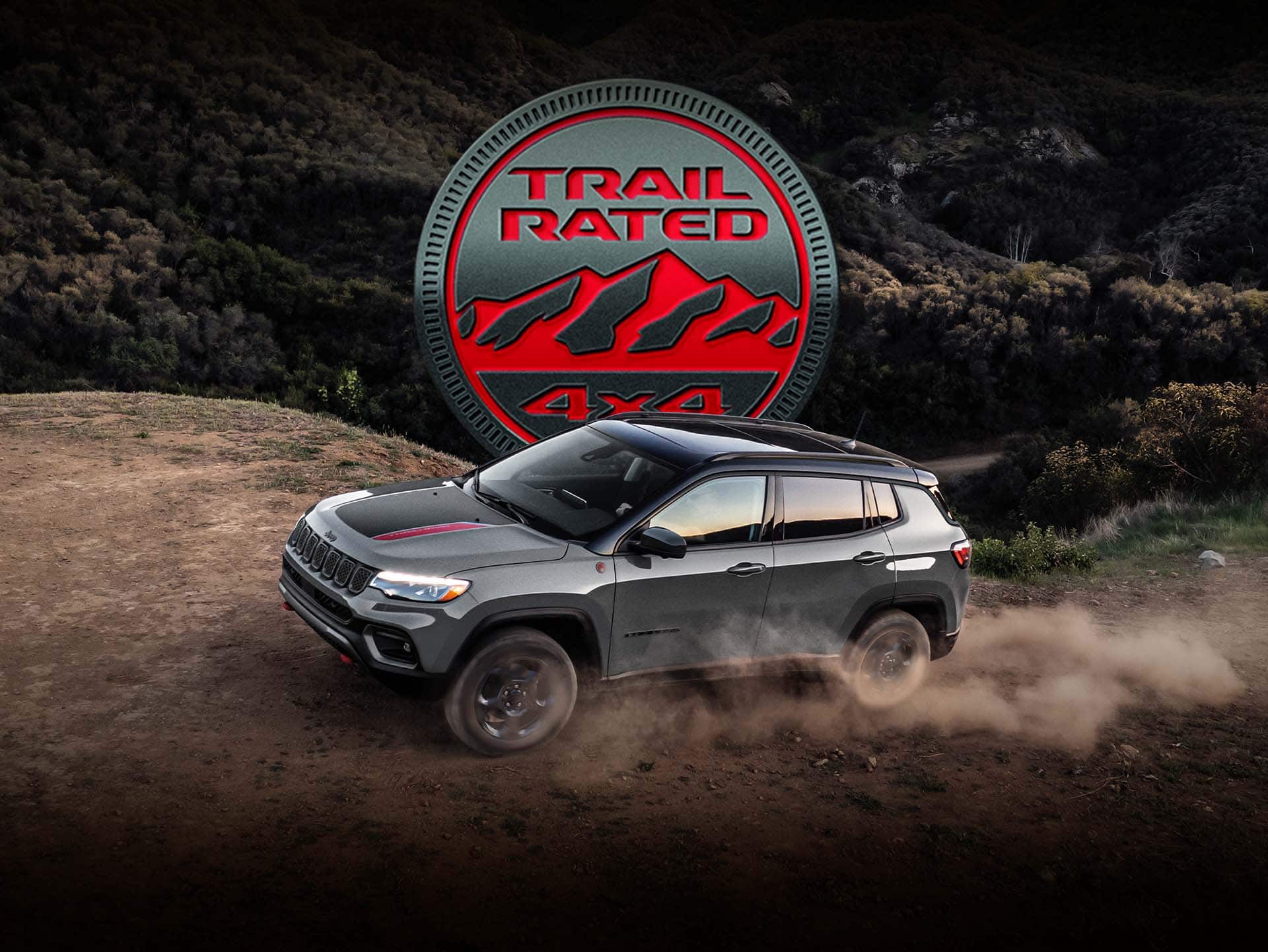 A 2023 Jeep Compass Trailhawk being driven on a hill off-road, with the tires kicking up dust. The Trail Rated 4x4 badge.