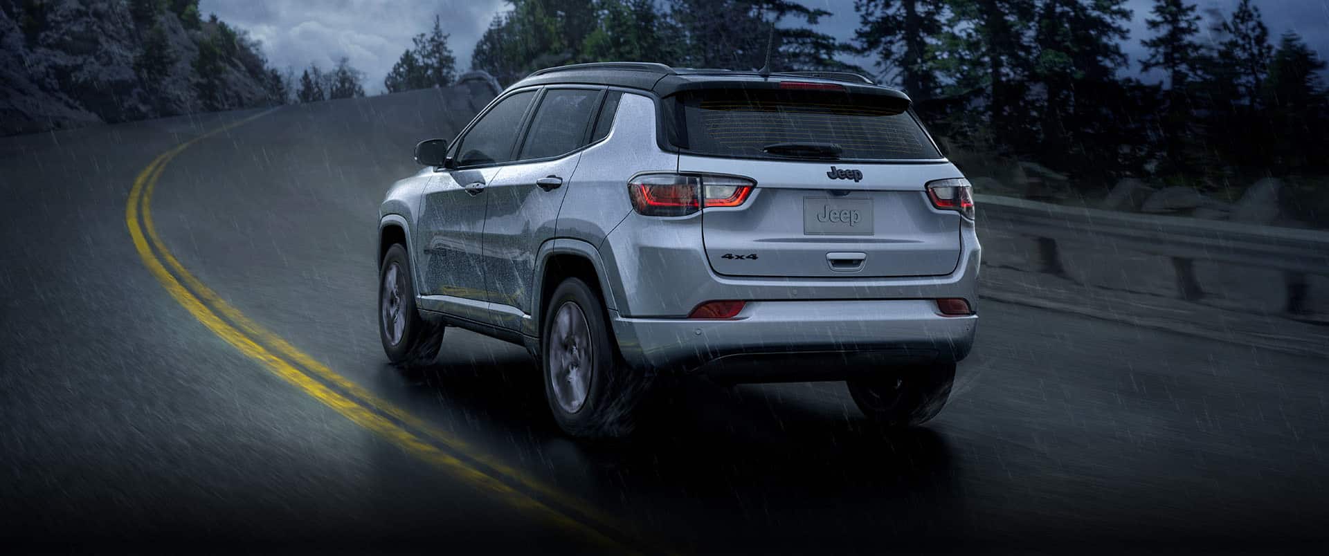 A rear view of a 2023 Jeep Compass High Altitude being driven on a winding highway during a rainstorm.