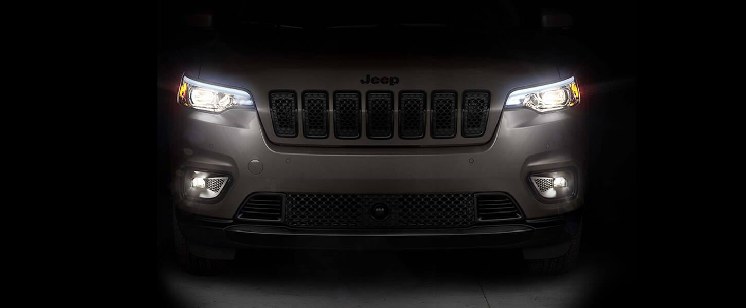 Vista frontal de un Jeep Cherokee Altitude Lux 2023 con sus faros delanteros y faros antiniebla encendidos.