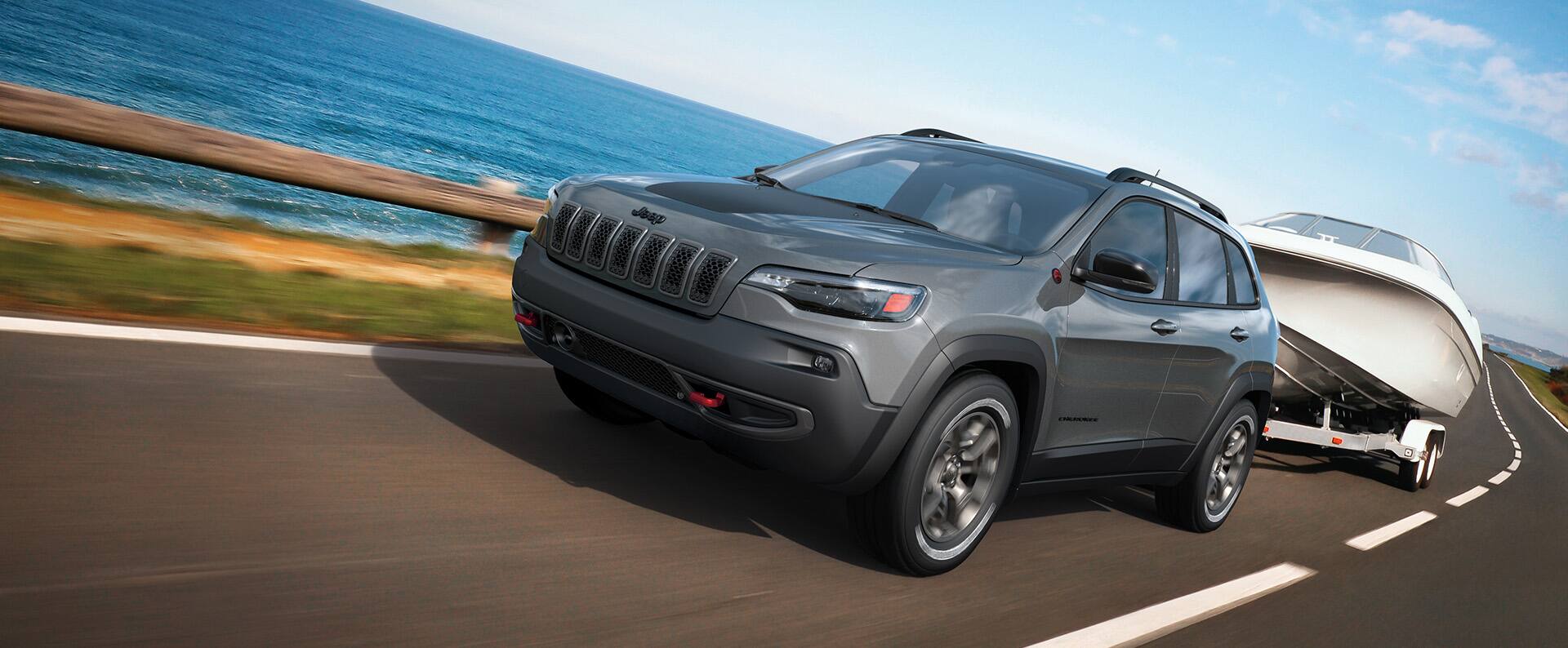 Un Jeep Cherokee Trailhawk 2023 remolcando una lancha motora, mientras circula por una autopista junto a una gran masa de agua.