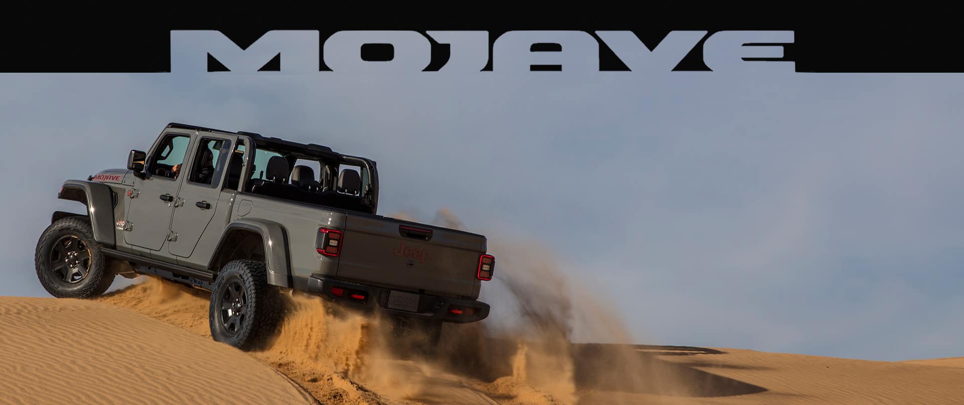 Mojave. The 2023 Jeep Gladiator Mojave being driven up a sand dune with a cloud of sand coming from its wheels.