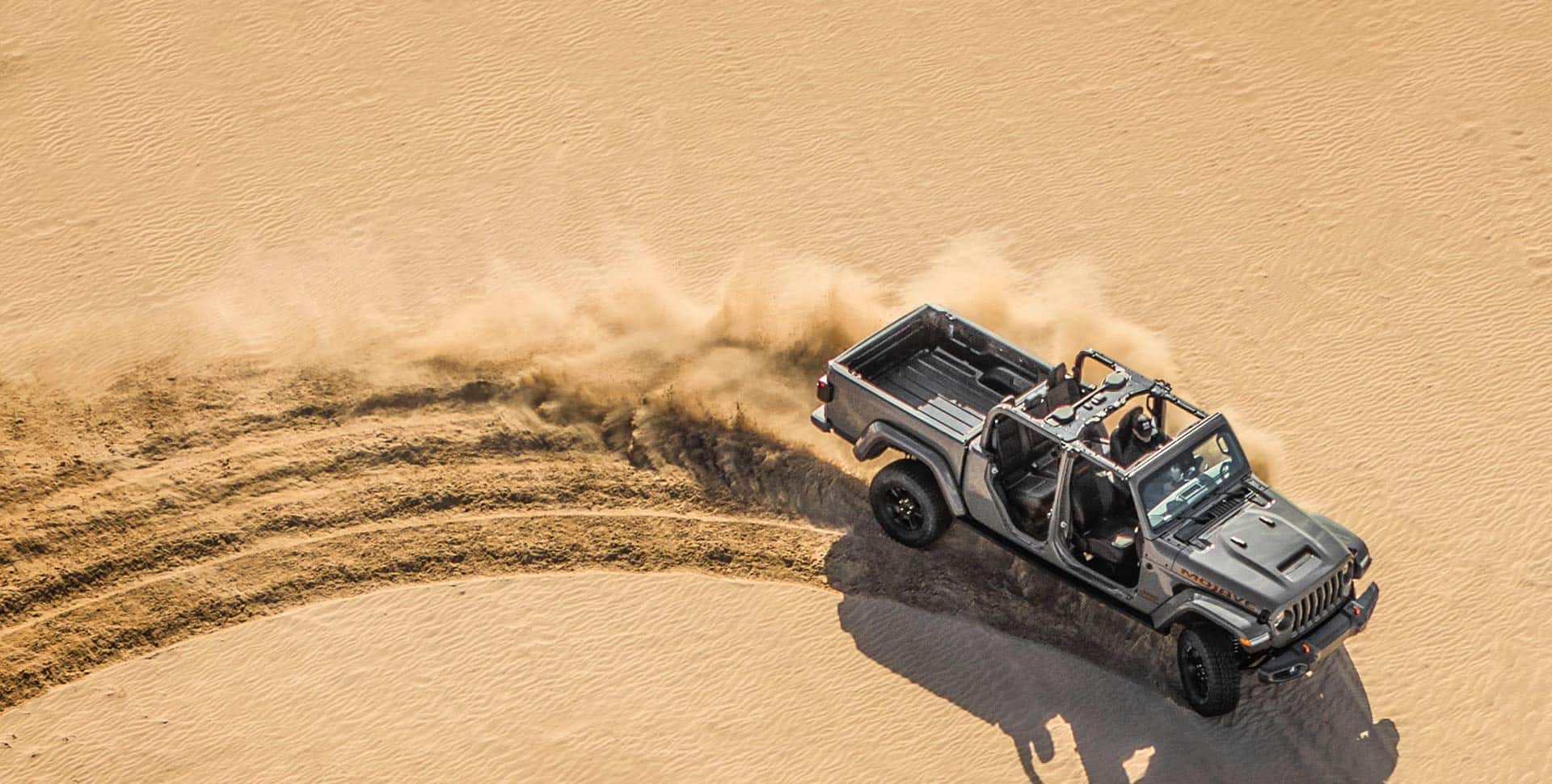 El Jeep Gladiator Mojave 2023 sin techo ni puertas, circulando en condiciones todoterreno, en el desierto, salpicando arena con las ruedas.