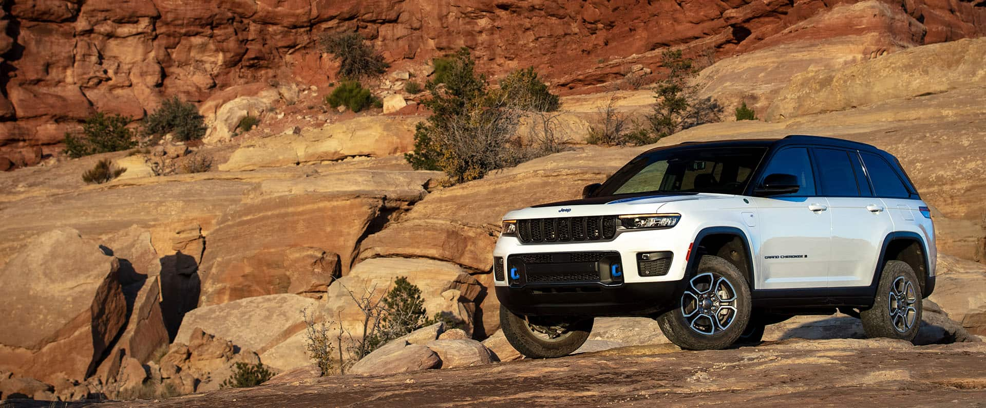 The 2023 Jeep Grand Cherokee Trailhawk 4xe parked on bare rock with a steep, rocky hill rising behind it.