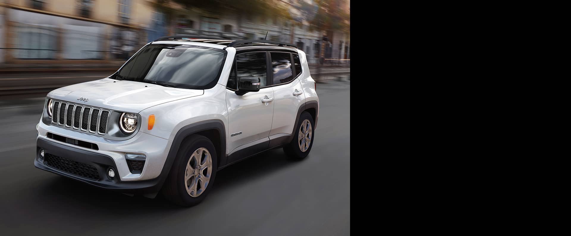 A white 2023 Jeep Renegade Limited being driven on a city street with the background blurred to indicate the speed of the vehicle.