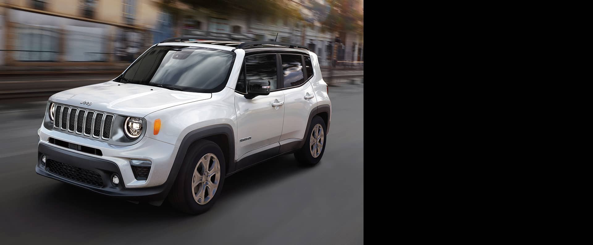 Un Jeep Renegade Limited 2023 blanco circulando por una calle de ciudad con el fondo difuminado para indicar la velocidad del vehículo.