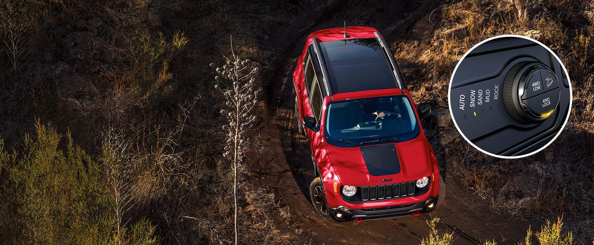 An overhead view of a red 2023 Jeep Renegade Trailhawk maneuvering through a muddy trail off-road. An insert close-up displays the five Selec-Terrain settings with "Snow" lit and the 4WD dial with "4WD Lock" lit.