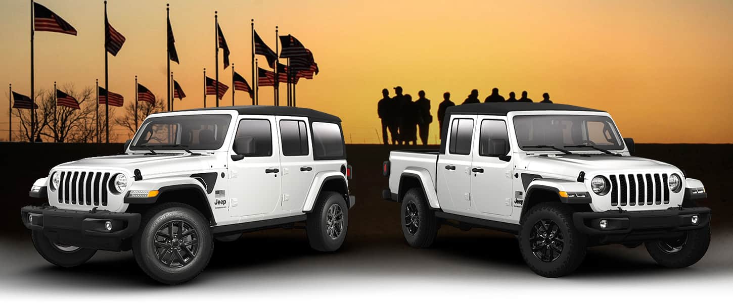 A white 2023 Jeep Wrangler Freedom Edition and white 2023 Jeep Gladiator Freedom Edition parked with a series of American flags and silhouetted military personnel standing in the background with a golden sky.