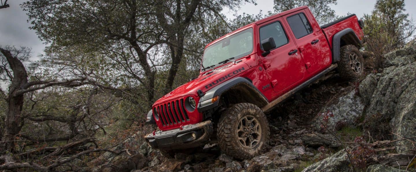 A red 2023 Jeep Gladiator Rubicon descending a steep hill of rocks, logs and tree roots.