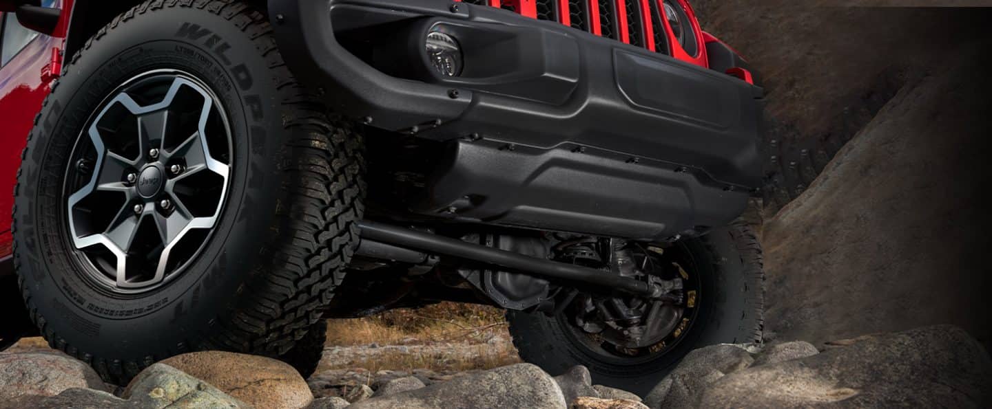 A close-up of the front wheels of the 2023 Jeep Gladiator Rubicon, each wheel at a different elevation due to the rocky terrain.