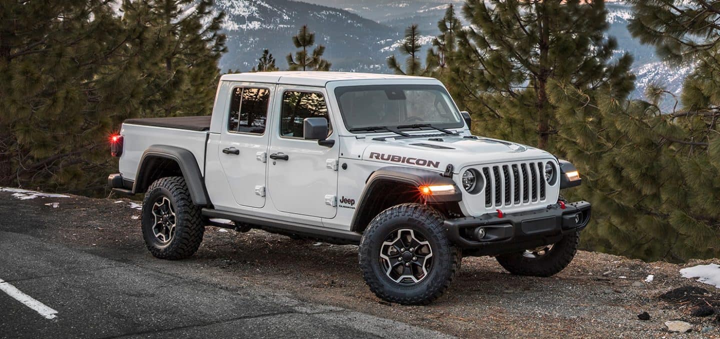 Display The 2023 Jeep Gladiator Rubicon, parked on a clearing beside large evergreens in the mountains.