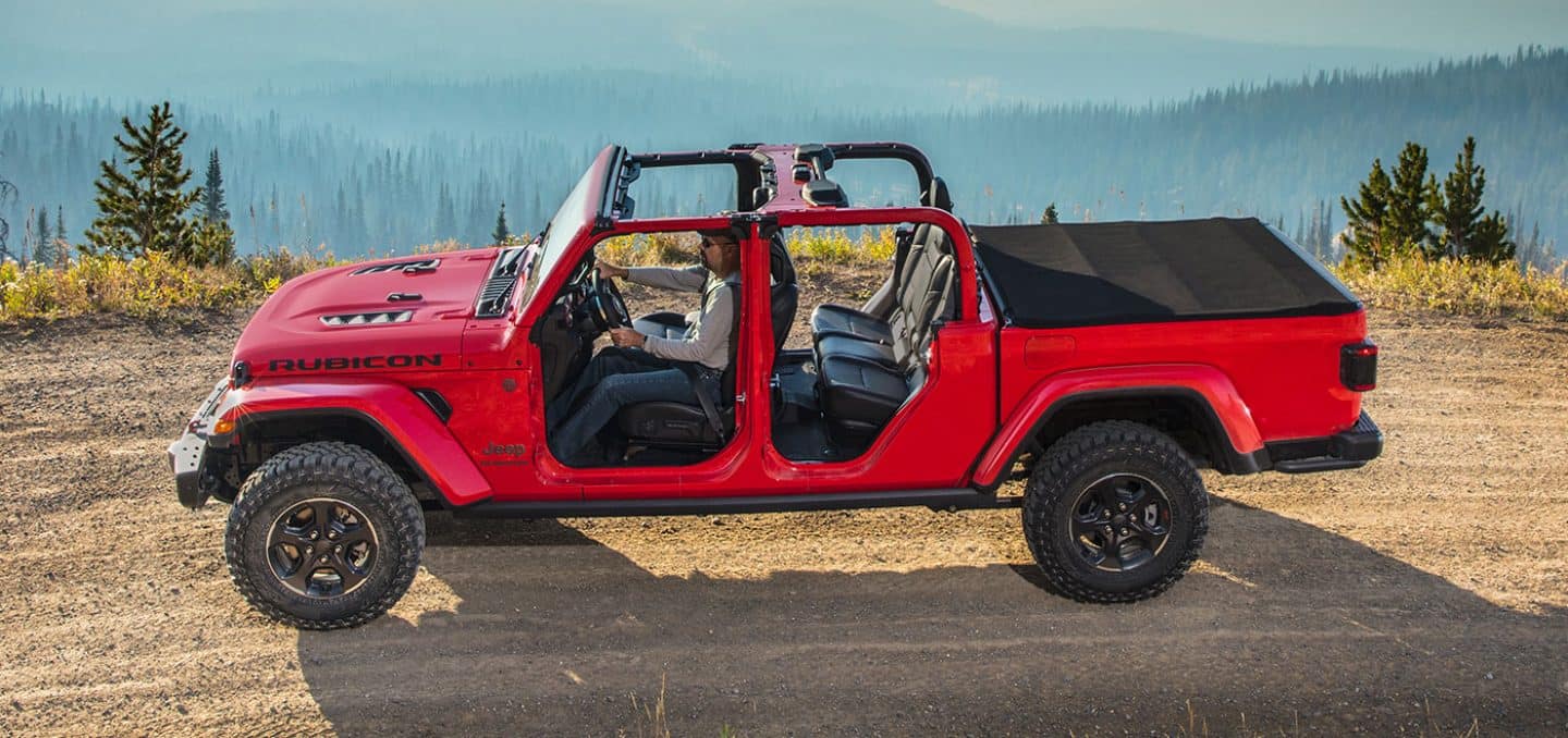 Display A profile view of a red 2023 Jeep Gladiator Rubicon with its tonneau cover fully closed and its doors and roof off.