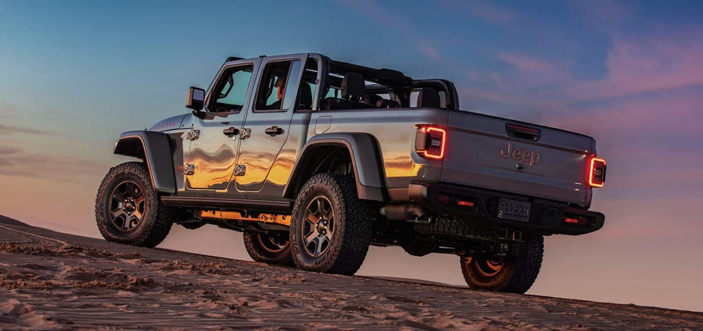 Display The 2023 Jeep Gladiator Mojave parked on a hill with the sunset reflected on its driver-side doors.