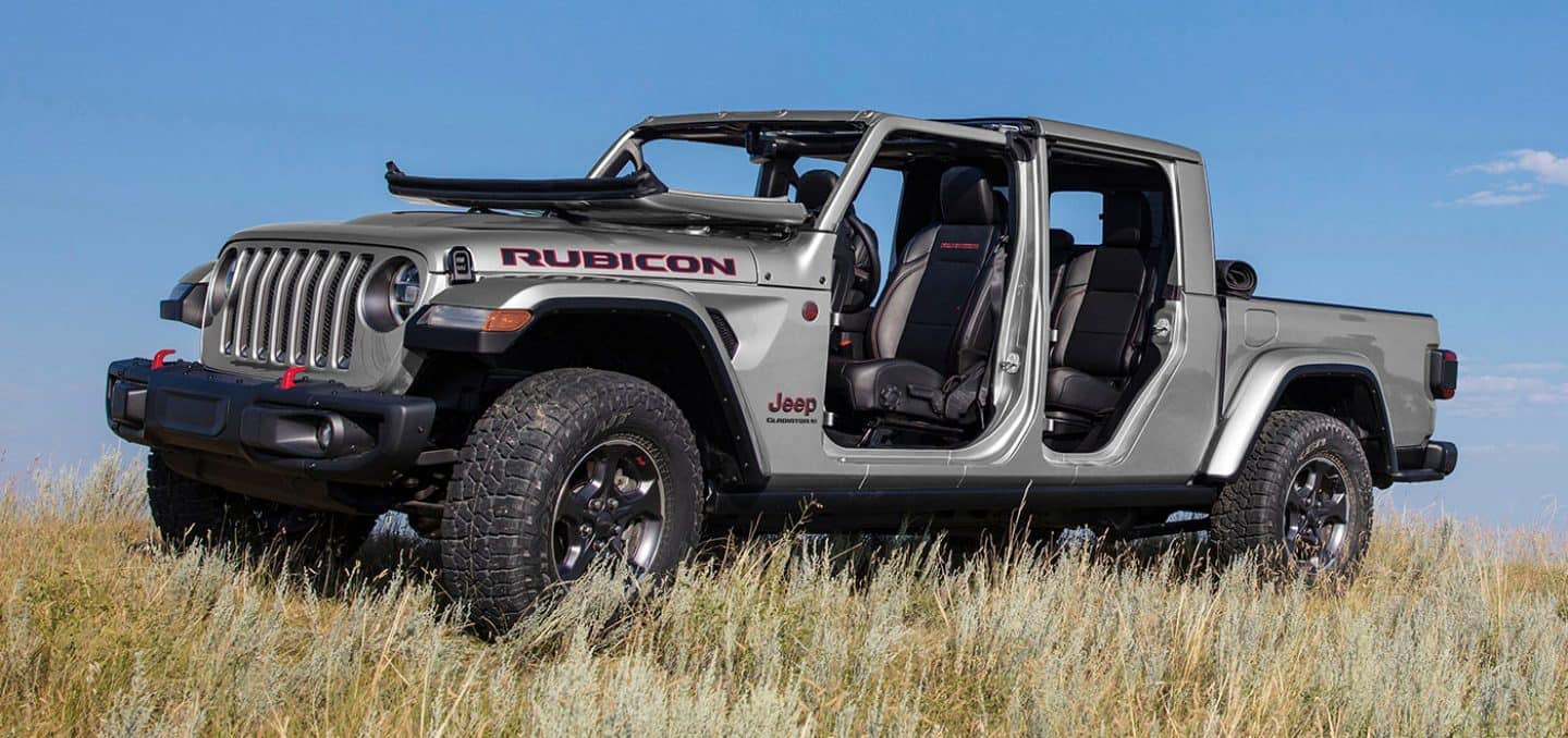 Display The 2023 Jeep Gladiator Rubicon with its windshield folded down and doors removed, parked off-road in tall grass.