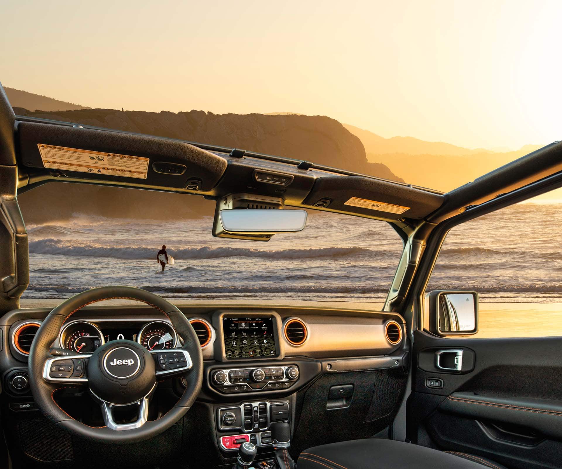The interior of the 2023 Jeep Gladiator Mojave with its top off, focusing on the ocean and sky visible through the windshield, open roof and open window.