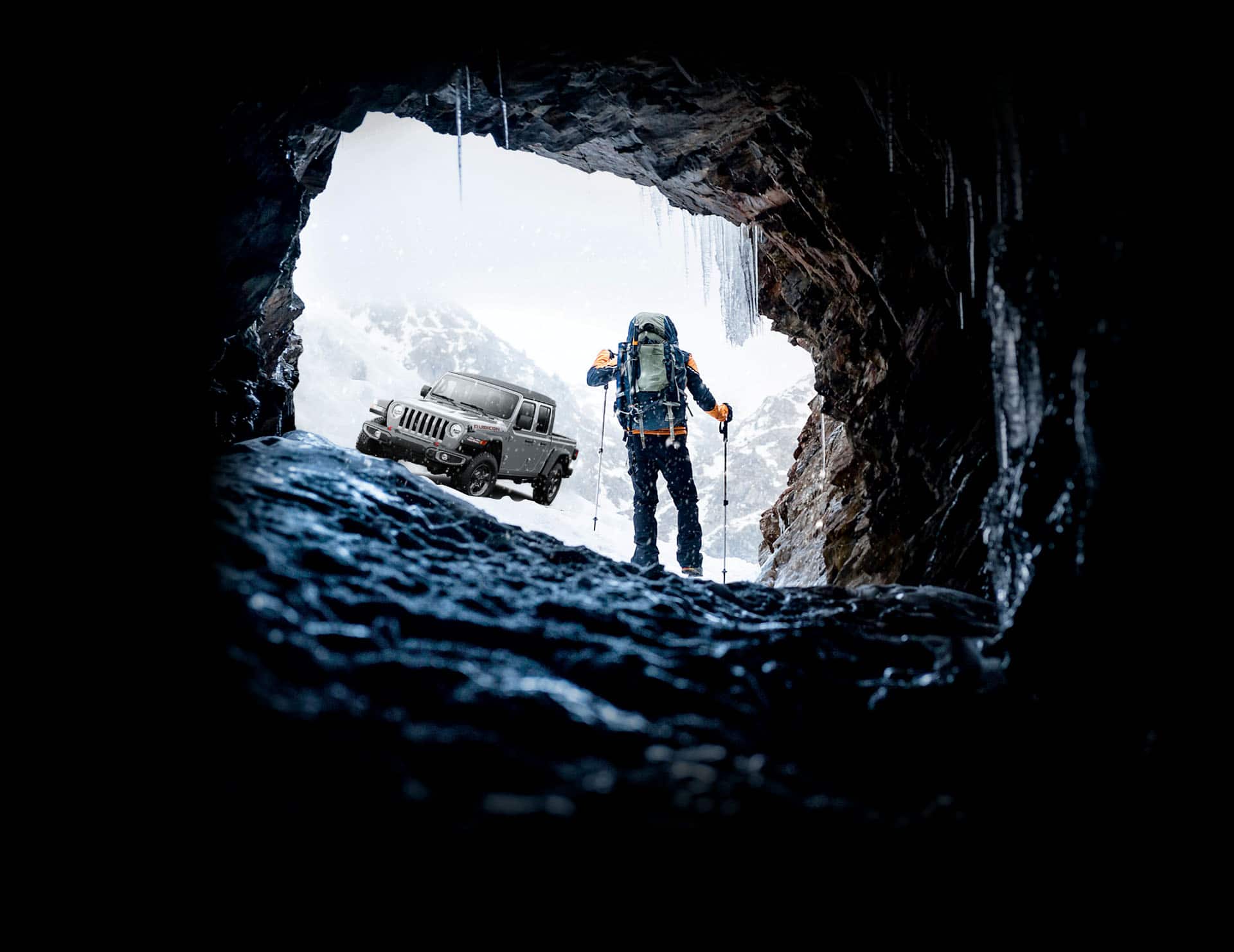 La Jeep Gladiator Rubicon 2023 estacionada mientras un alpinista camina hacia ella emergiendo de una gélida caverna en las montañas nevadas.