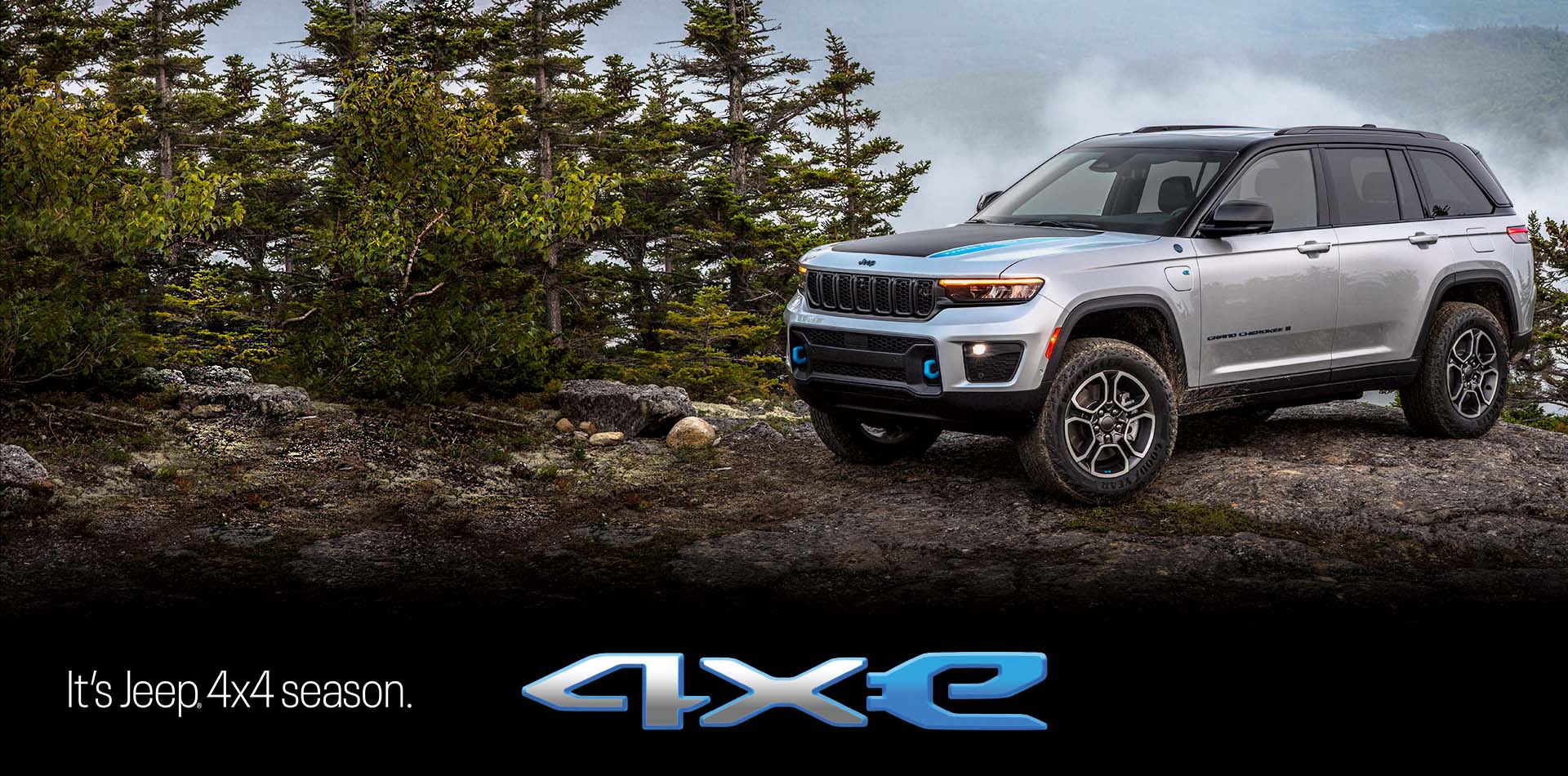 A silver 2023 Jeep Grand Cherokee Trailhawk 4xe parked on a rocky outcropping in a forest, with mountains surrounded in fog in the background. Grand Cherokee. The It's Jeep Season logo.