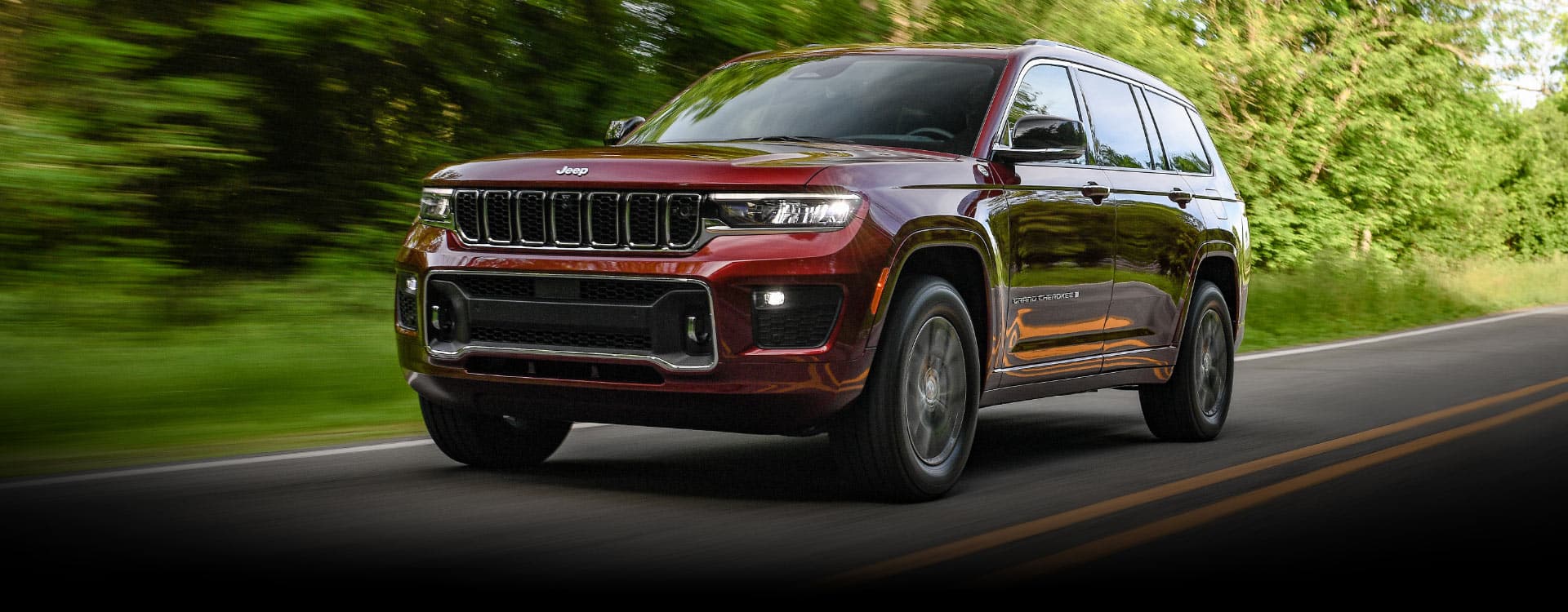 El Jeep Grand Cherokee Overland 2023 circulando por una carretera, con árboles borrosos en segundo plano, que sugieren la velocidad del vehículo.