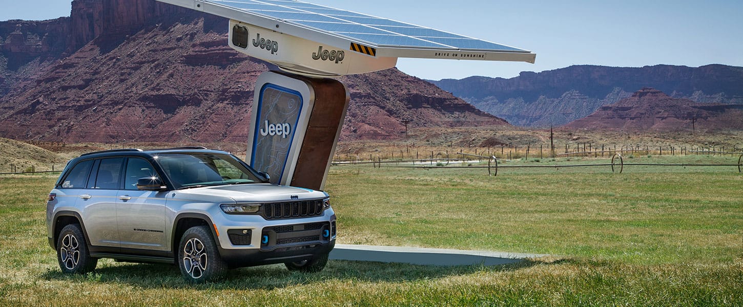 The 2023 Jeep Grand Cherokee 4xe parked at a Jeep-branded charging station at a trailhead.