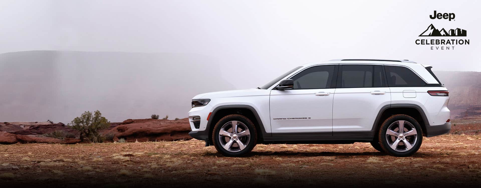A driver-side profile of a white 2023 Jeep Grand Cherokee Limited parked on a trail off-road. The Jeep Celebration Event.