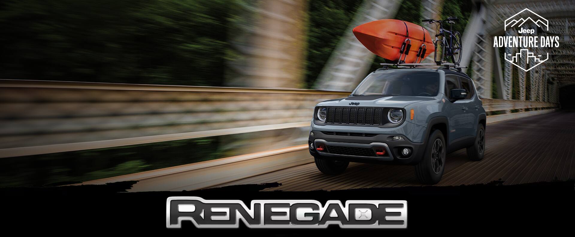 A blue 2023 Jeep Renegade Trailhawk being driven across a suspension bridge at night with a kayak and bike strapped to its roof rack. Jeep Adventure Days logo. Renegade.