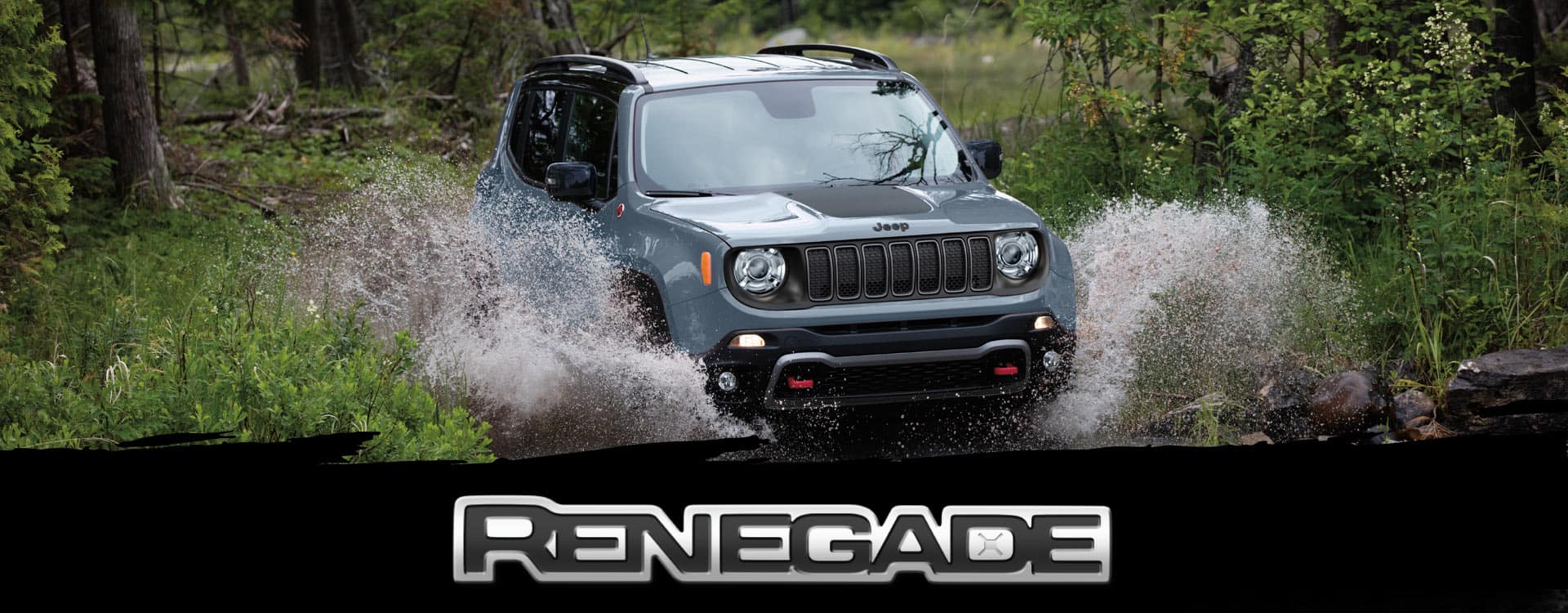 A blue gray 2023 Jeep Renegade Trailhawk fording through a narrow creek off-road, with water spraying above the vehicle's wheel wells. Renegade.