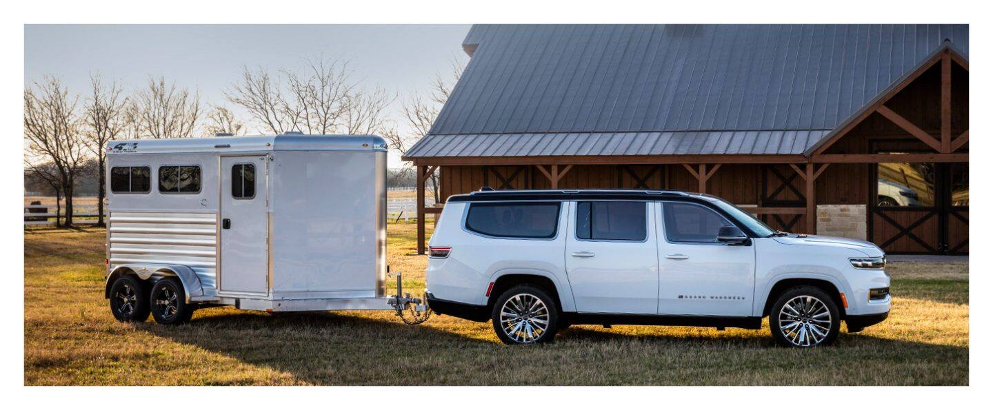 A profile of the 2023 Grand Wagoneer Series III parked in front of a barn with a small enclosed trailer in tow.