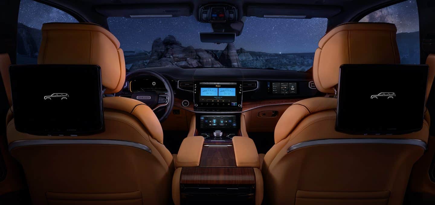 Display The interior of the 2023 Grand Wagoneer Series III with the Uconnect touchscreen showing the audio settings and a view through the windshield of a starry sky.