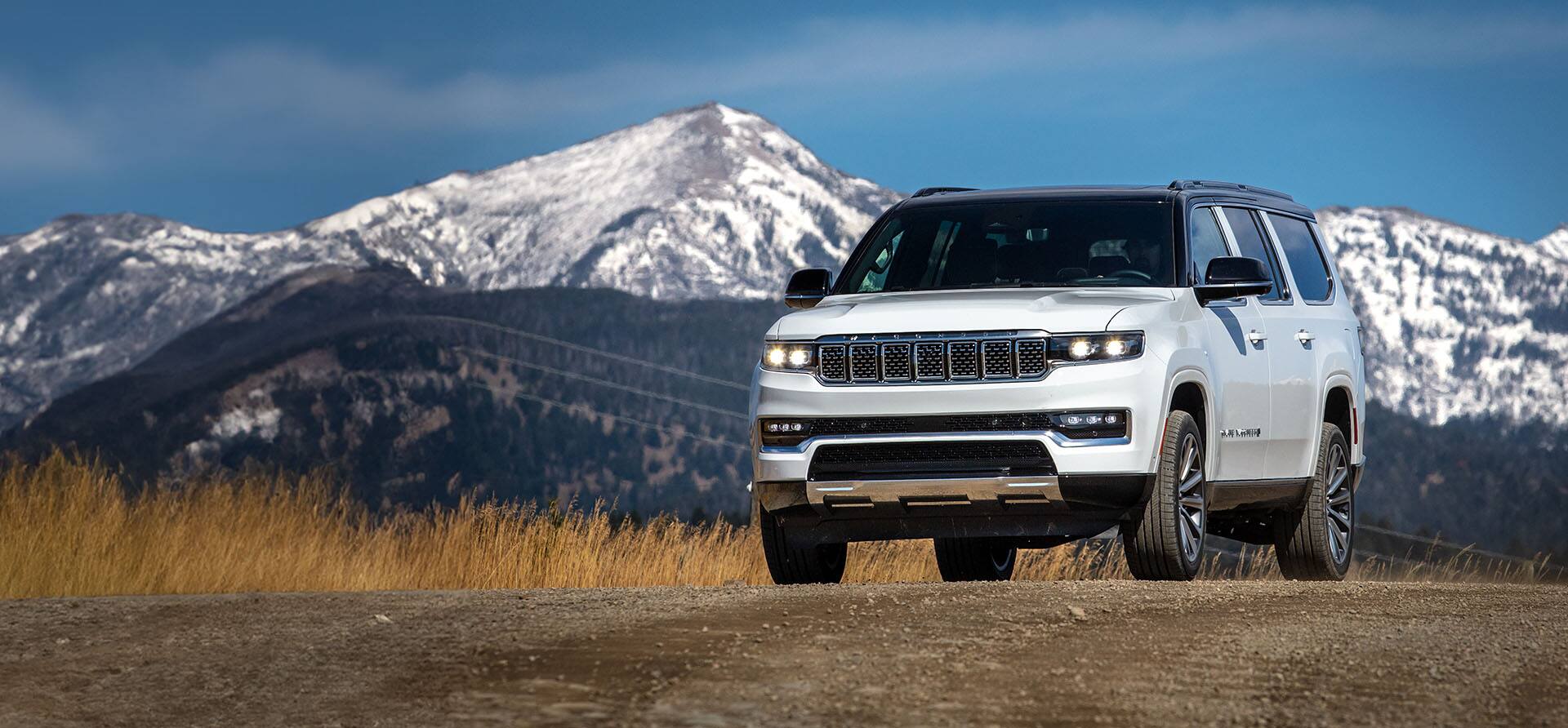 An angled front profile of a white 2023 Grand Wagoneer Series II parked on a clearing with mountains in the background.