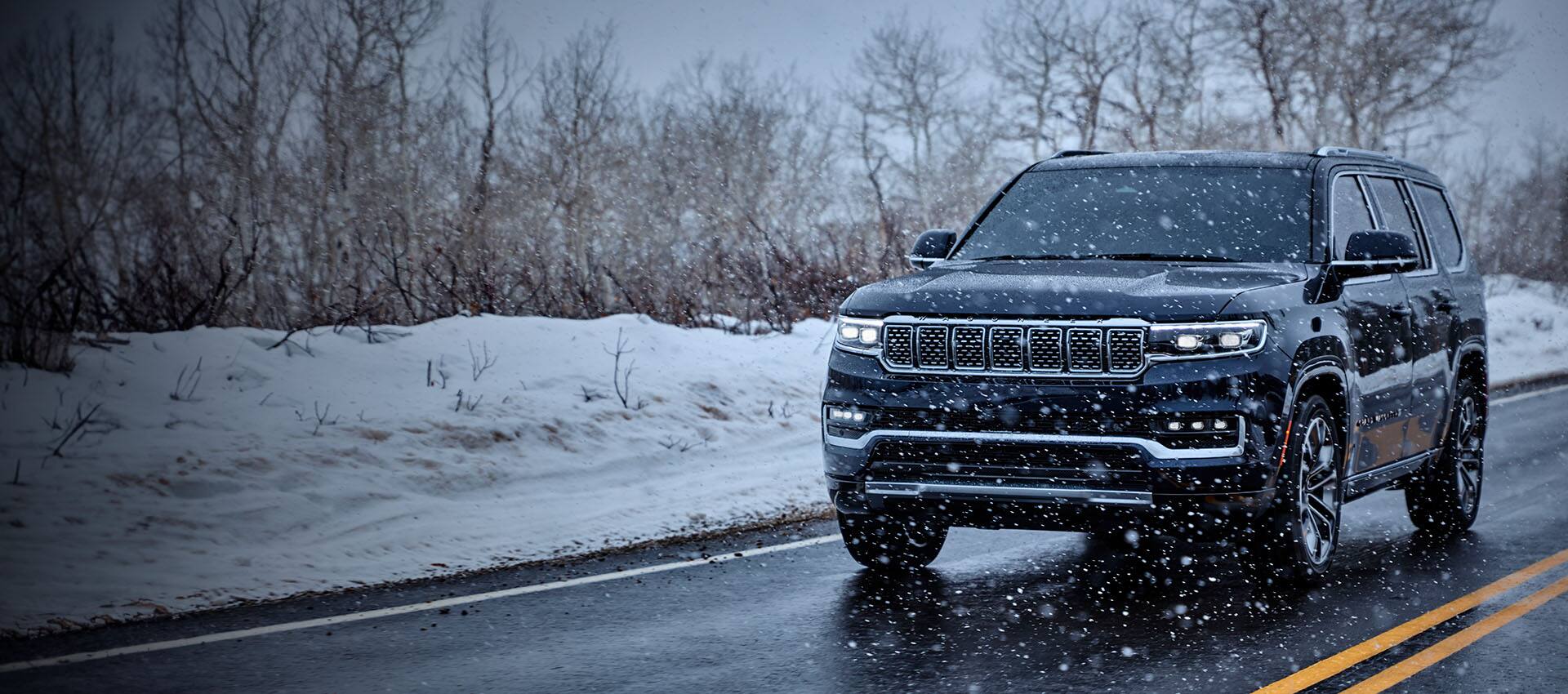 A blue 2023 Grand Wagoneer Series III being driven through a snowstorm on a two-lane highway.