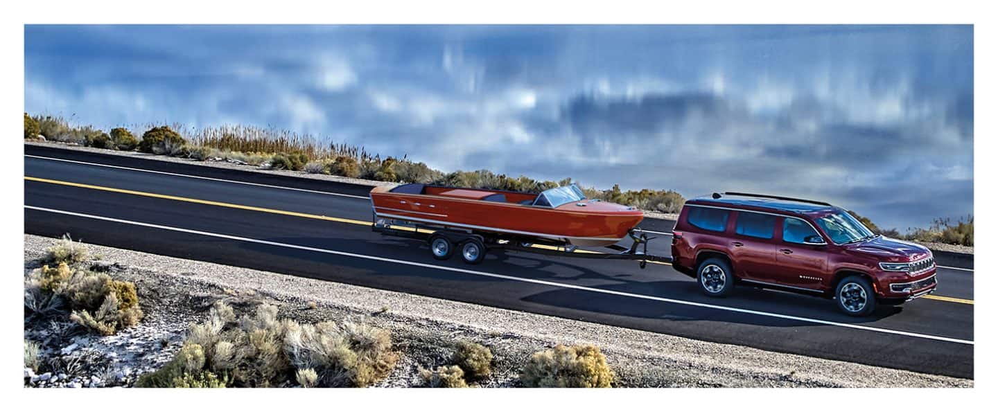 The 2023 Wagoneer Series III towing a motorboat on a lakeside road.