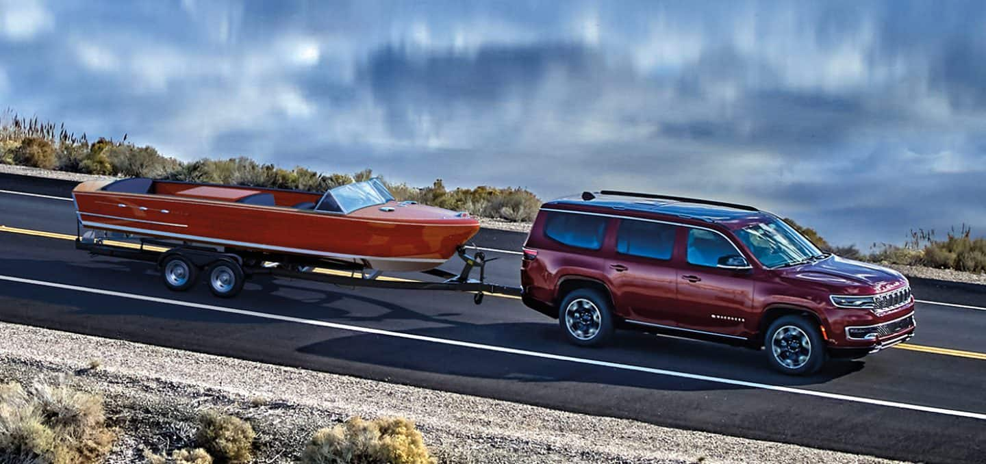 2023 Red Jeep Grand Wagoneer towing a red boat alongside a lake