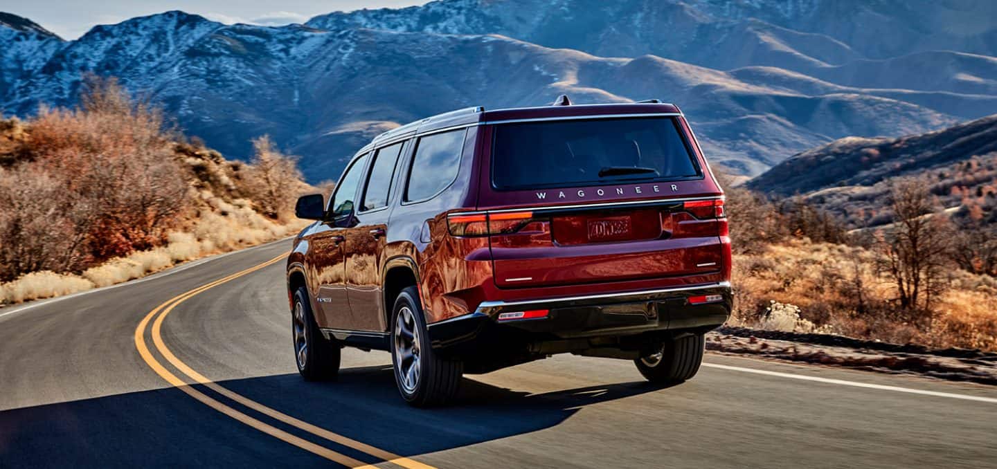 Display A rear view of the 2023 Wagoneer Series III as it is driven on a winding road toward the mountains.