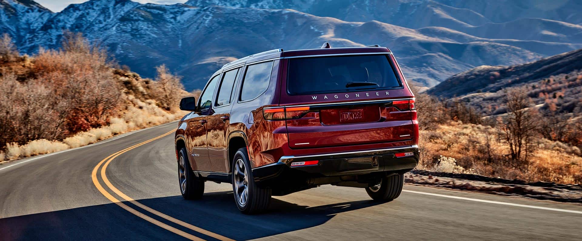 The rear view of the 2023 Wagoneer Series III being driven on a winding road in the mountains.