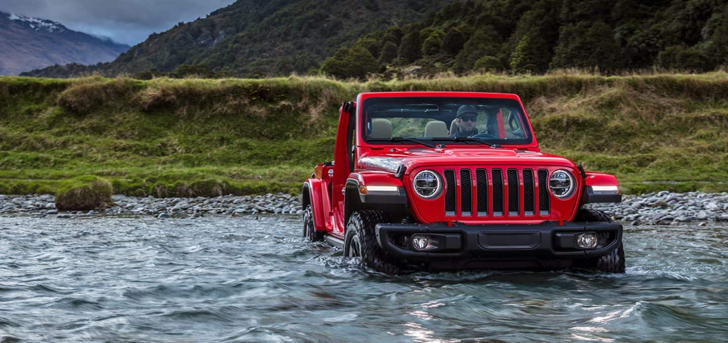 2023 Jeep Wrangler Rubicon in red driving through a mountain stream