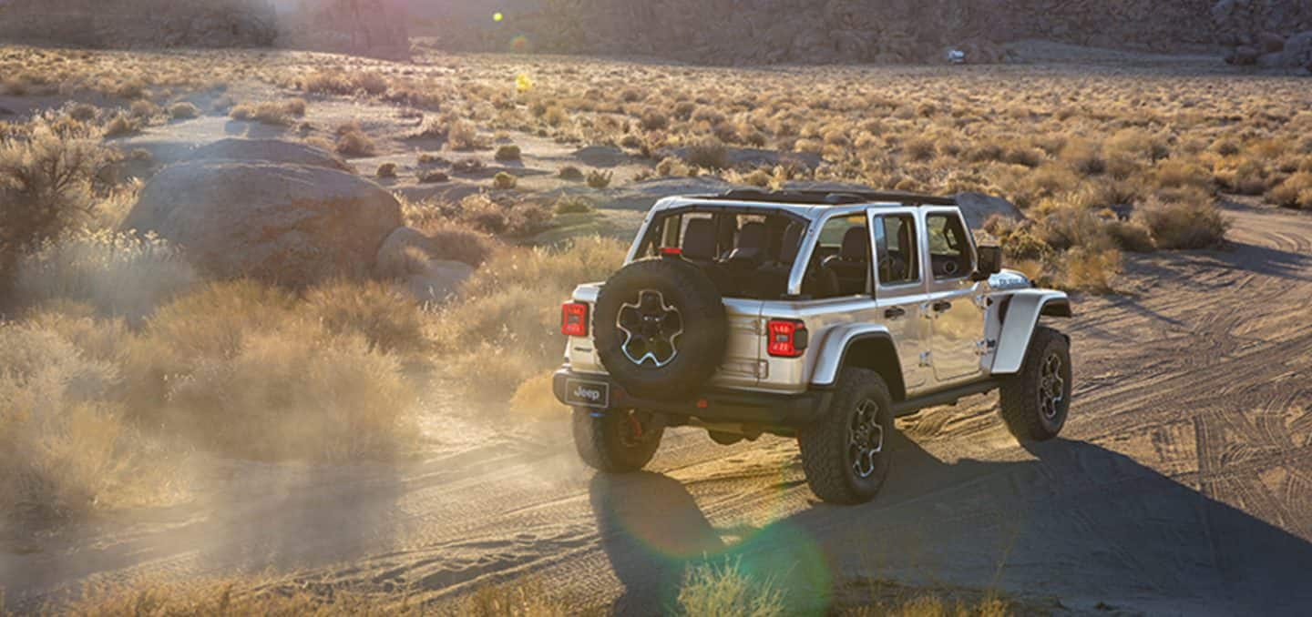 2023 Jeep Wrangler Rubicon in silver driving through a desert landscape with scrub grass in the background