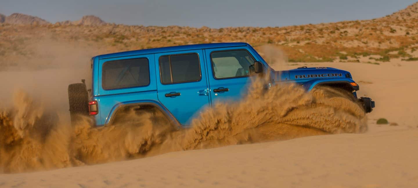 The 2023 Jeep Wrangler Rubicon 392 being driven off-road in deep sand, with a cloud of dust completely obscuring its wheels.