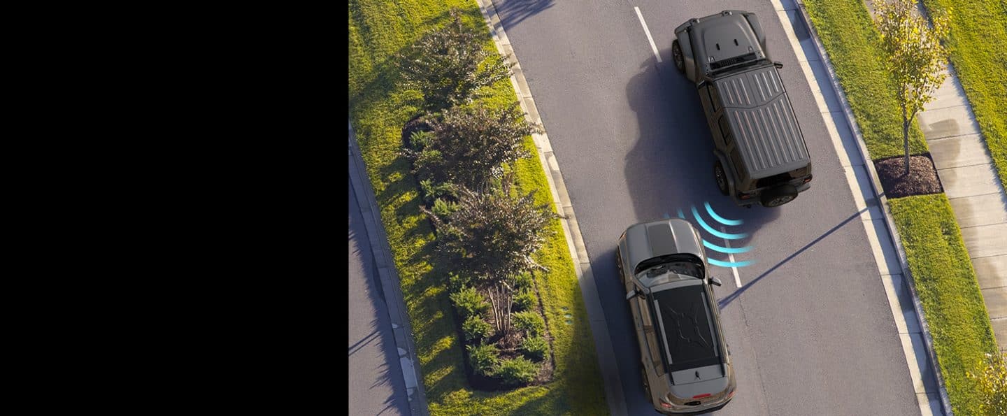 An overhead view of the 2023 Jeep Wrangler Overland with illustrated sensor bars coming from its rear and detecting a vehicle approaching in the next lane.