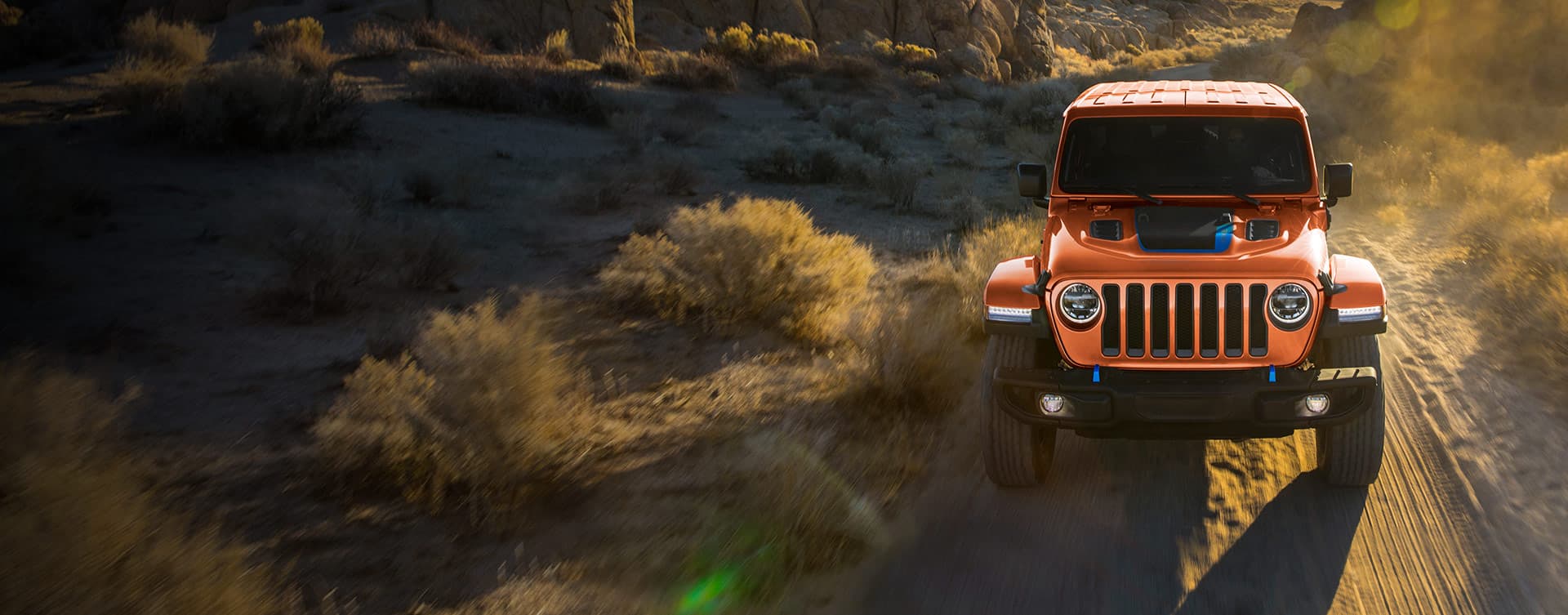 An orange 2023 Jeep Wrangler Rubicon 4xe with the Punk'n limited edition color being driven down a scrubby trail off-road.
