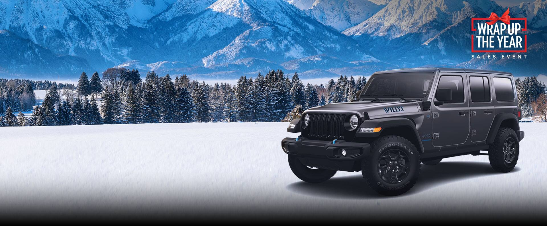 Un perfil desde el ángulo del conductor de un Jeep Wrangler Willys 4xe 2023 gris estacionado en la nieve, con árboles de hoja perenne y montañas de fondo. Evento de ventas de Fin de año.