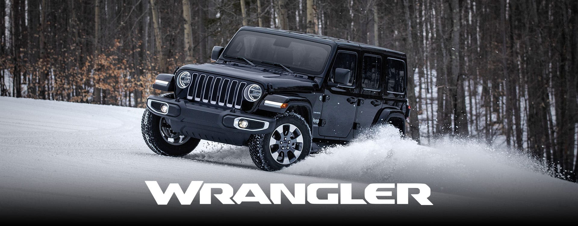A black 2023 Jeep Wrangler Sahara four-door being driven through a snow-covered trail off-road, in the woods. Wrangler.