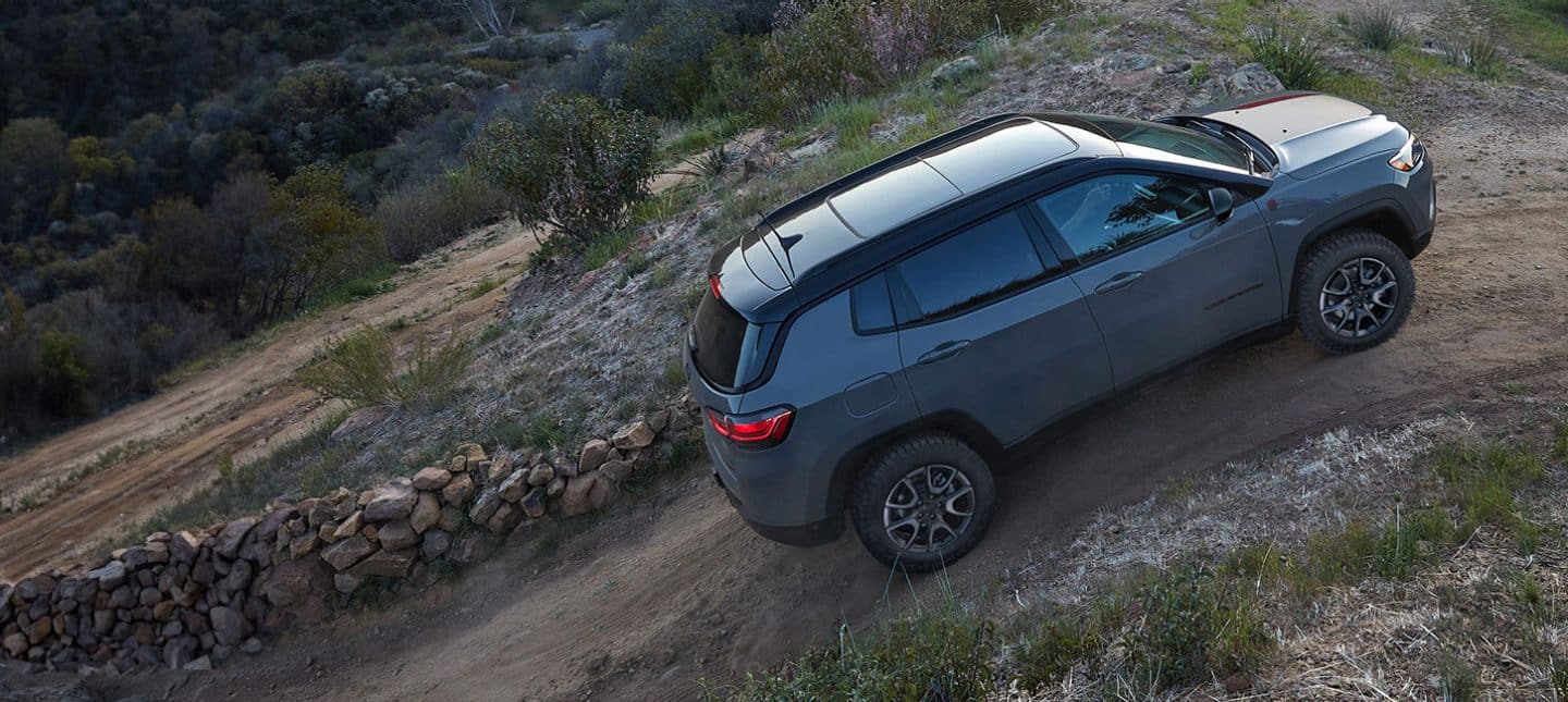 Un Jeep Compass Trailhawk 2024 asciende por un empinado camino de tierra junto a un cerco de piedras.