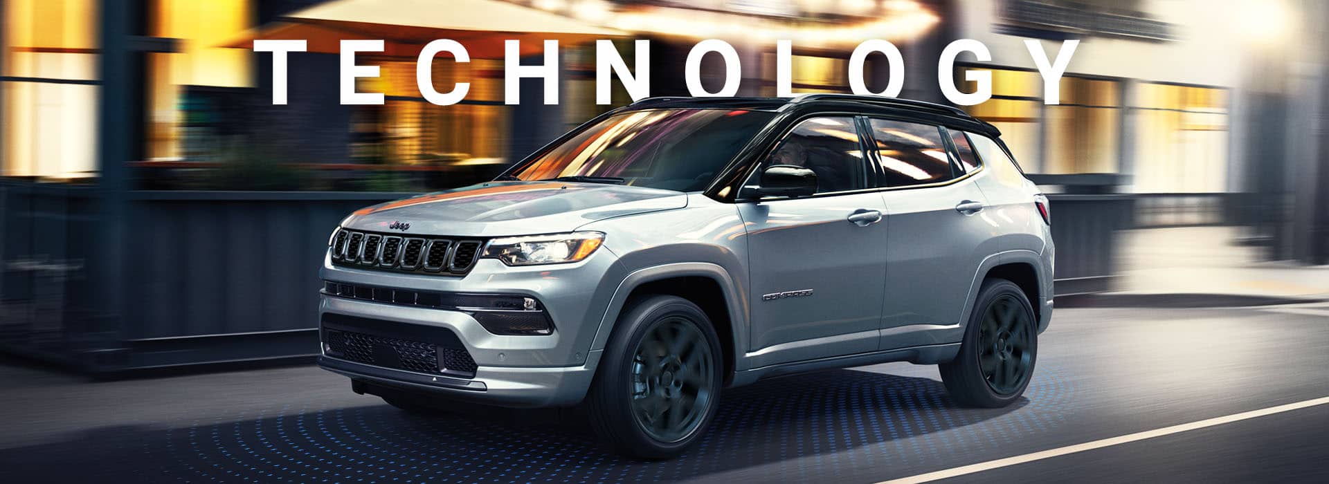 Un Jeep Compass High Altitude 2024 anda de noche por la calle de una ciudad, con el fondo difuminado para indicar que el vehículo está en movimiento. Tecnología.