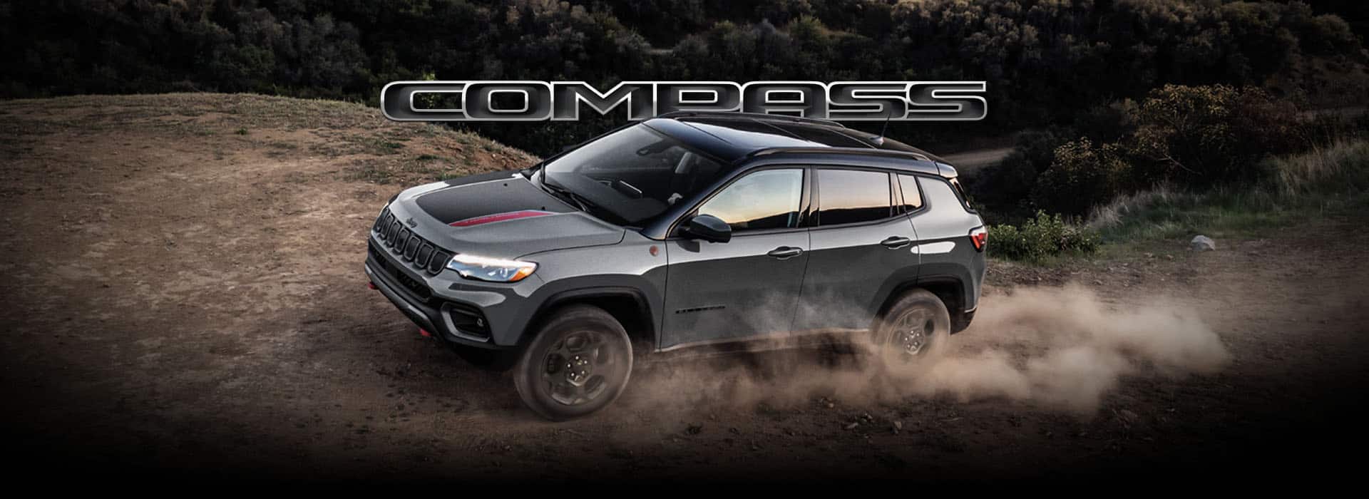 A 2024 Jeep Compass Trailhawk being driven on a hill off-road, with the tires kicking up dust. Compass.