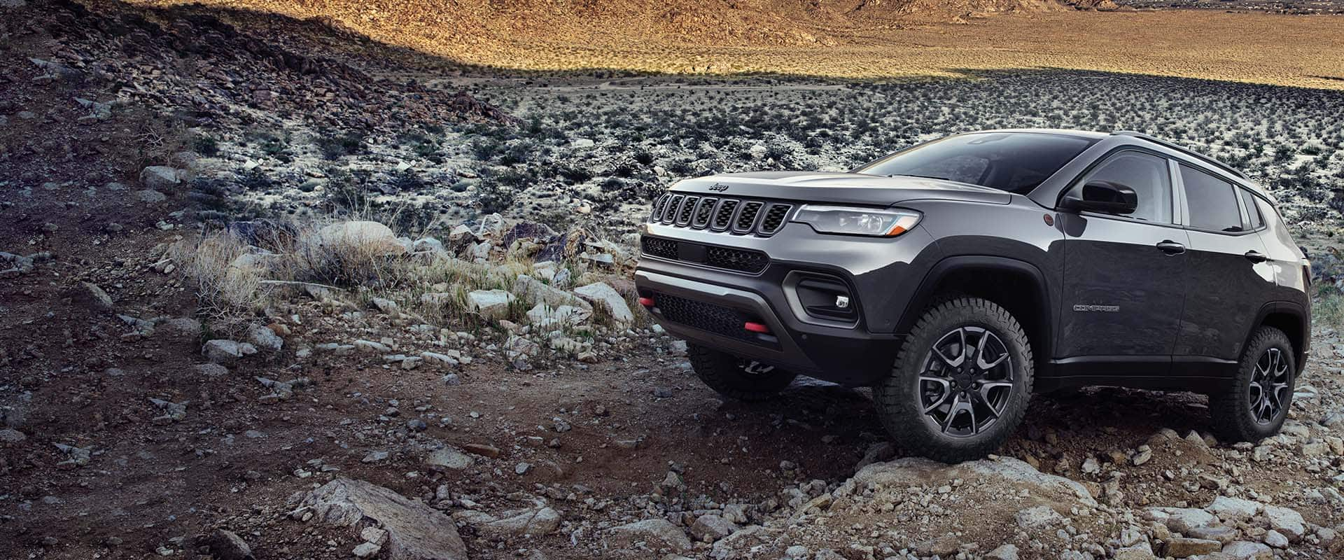 Un Jeep Compass Trailhawk 2024 gris atravesando rocas y piedras grandes y pequeñas en un camino fuera de la carretera.