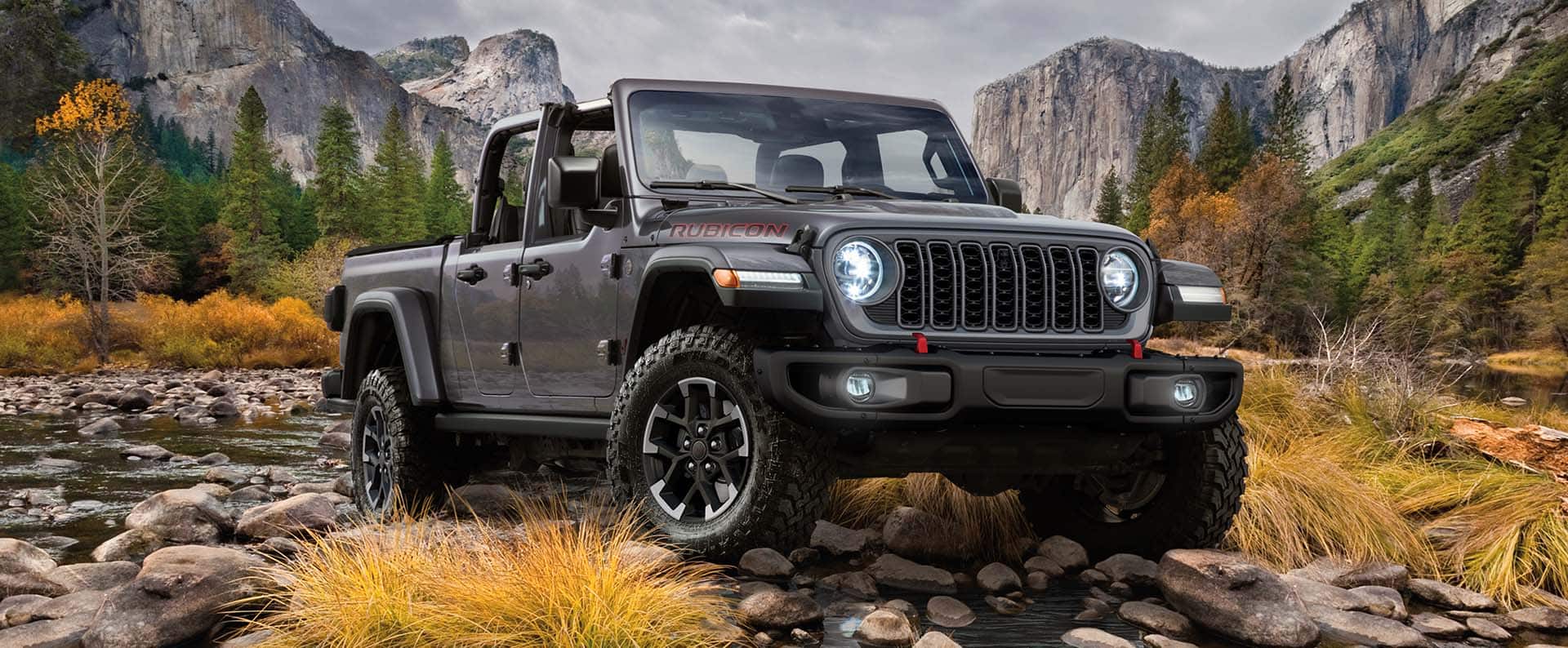 Una Jeep Gladiator Rubicon 2024 saliendo de un arroyo todoterreno con montañas de fondo.