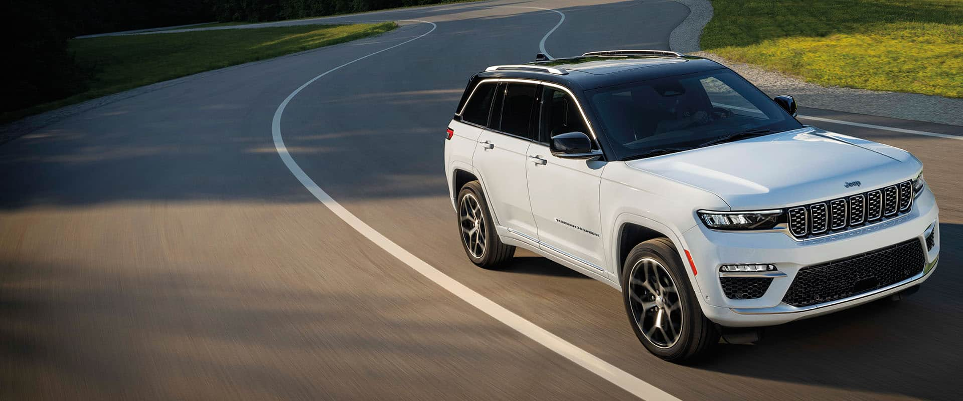 Un Jeep Grand Cherokee Summit Reserve 2024 blanco circulando por una carretera con curvas.